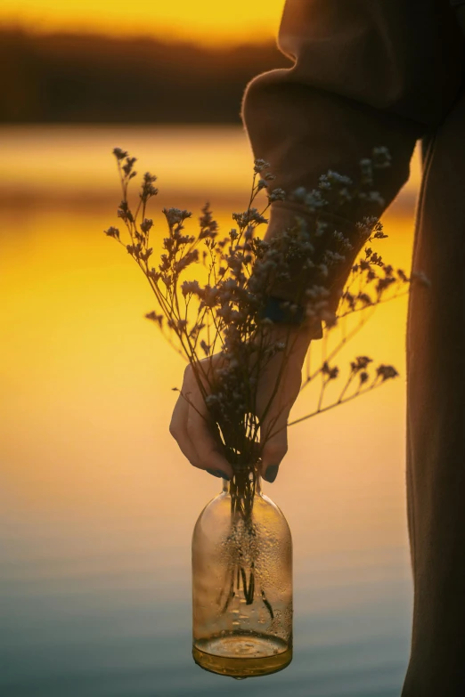 the person is holding flowers in a glass jar with water