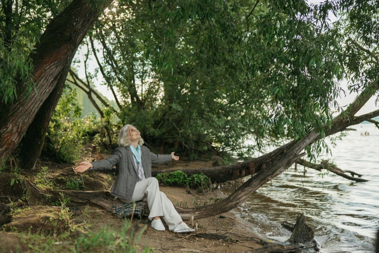 a woman is sitting under a large tree by the water