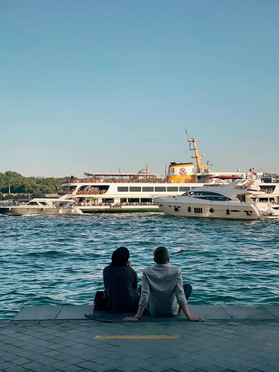 two people sit on a dock looking at the water