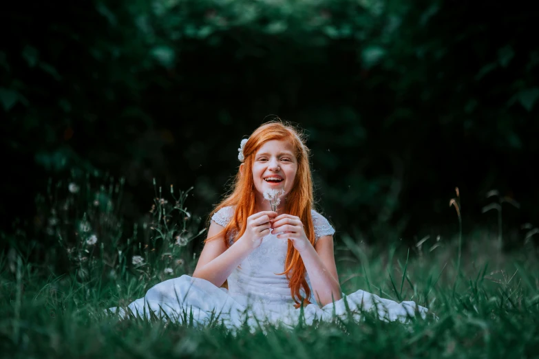 a little red headed girl with frecky hair on her knees sitting in grass