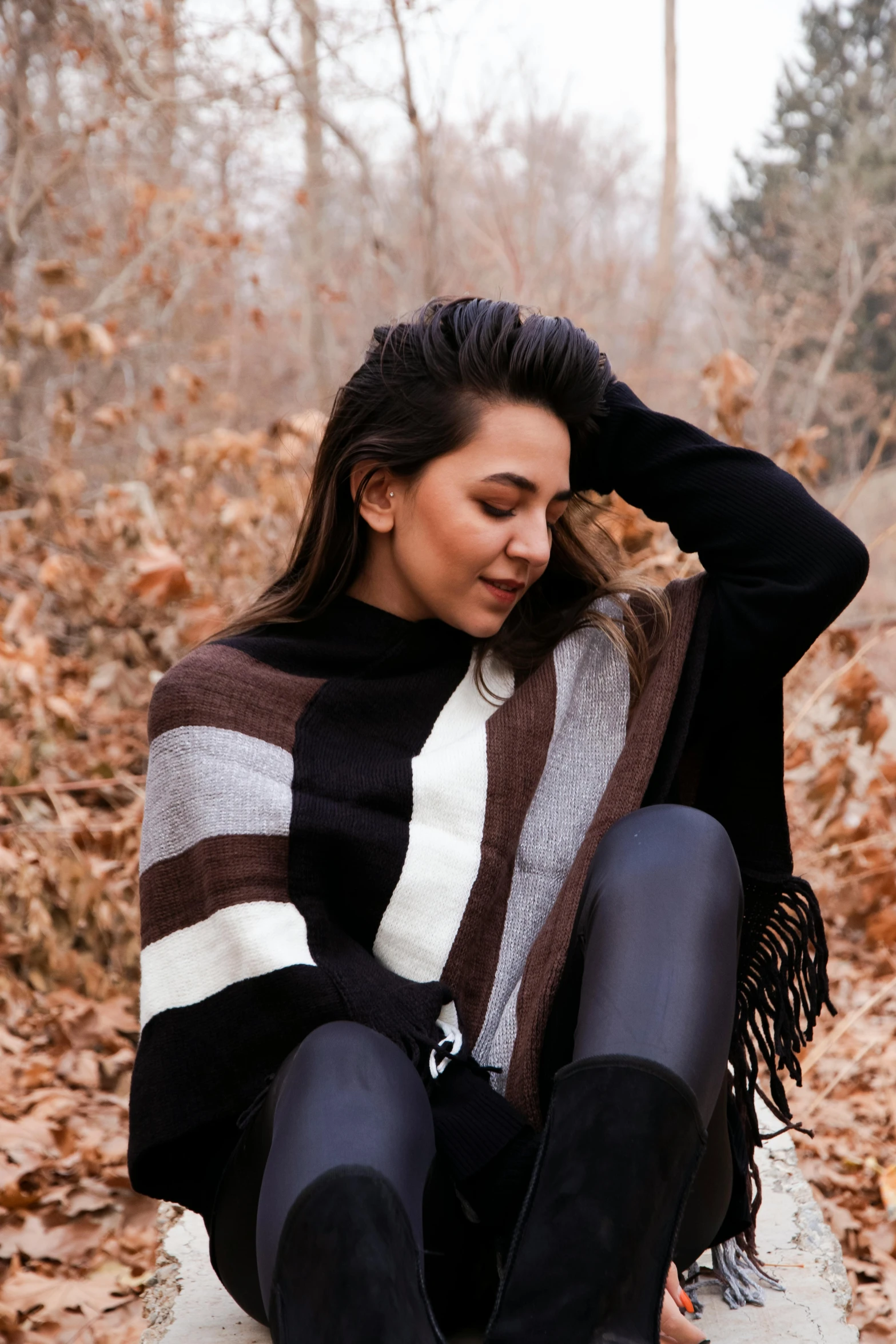 a woman sitting in a leaf covered forest wearing a striped sweater