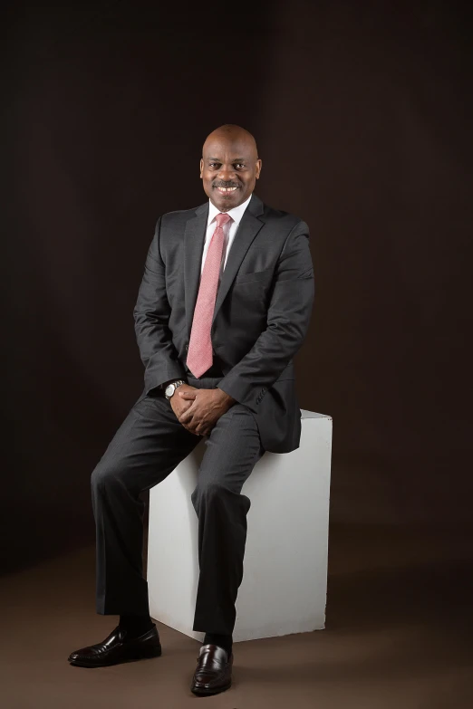 man posing for portrait wearing red tie, black suit and slip on shoes