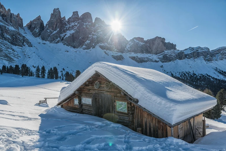 the sun shining behind a mountain hut, surrounded by snow