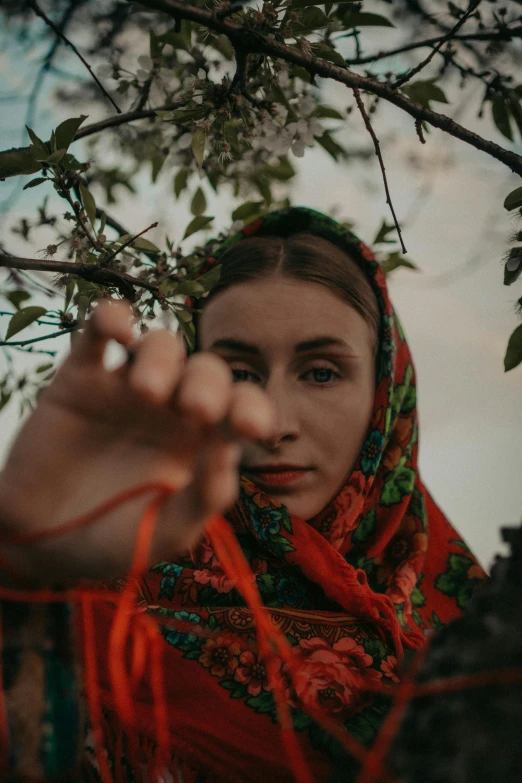 a woman wearing an orange scarf standing under a tree