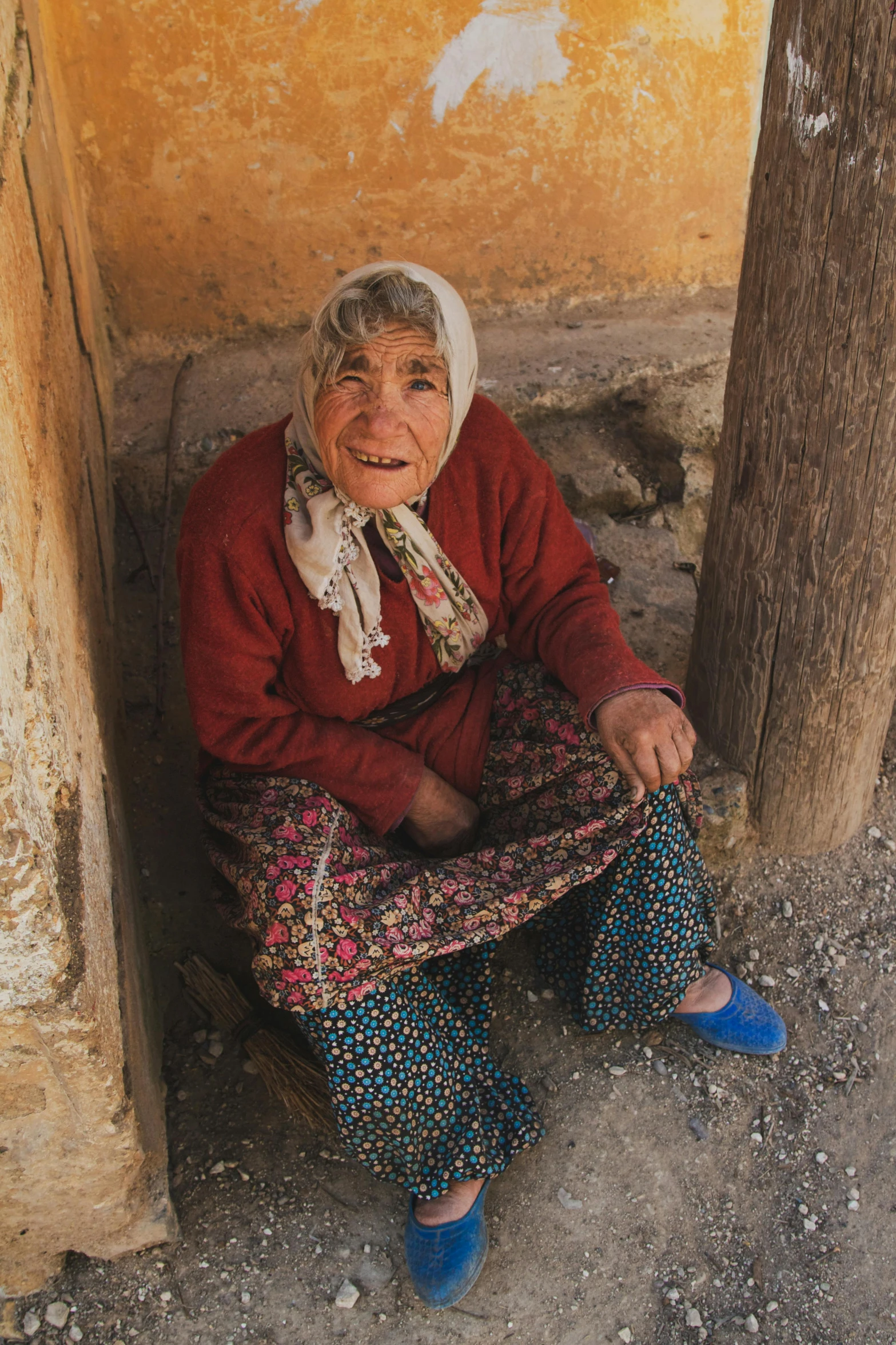 an older woman sits on the ground in front of an old house