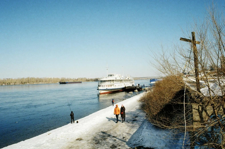 two people walking on snow near a river