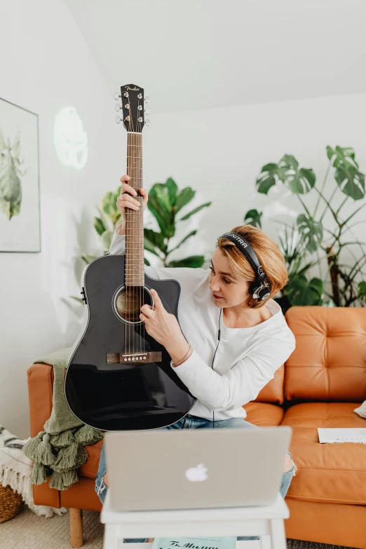 a woman sitting on a couch playing a guitar with headphones