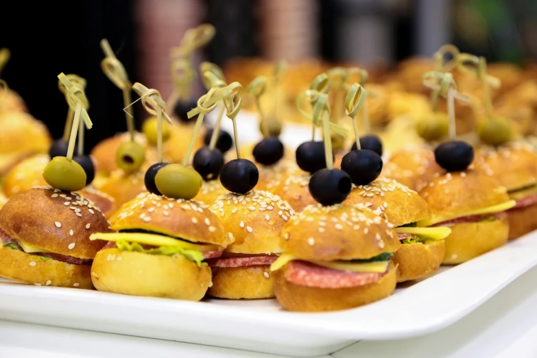 many small sandwiches on a plate that have olives in them