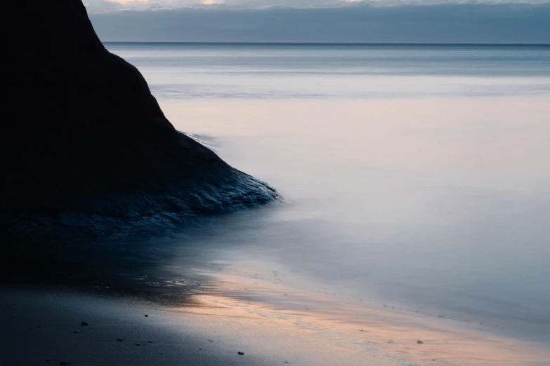 a body of water near a mountain under a cloudy sky