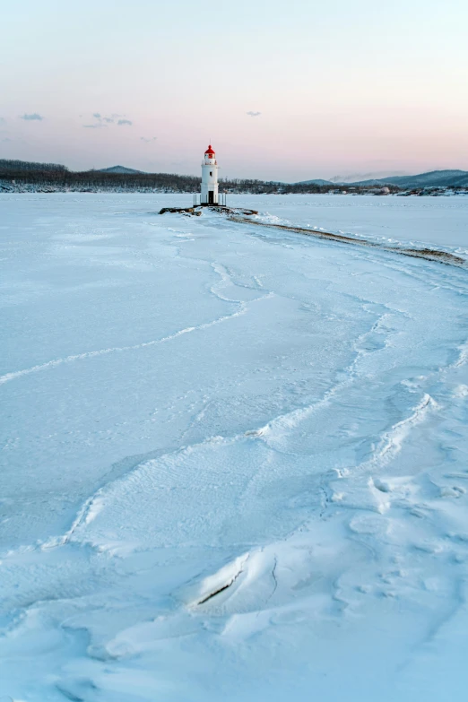 a lighthouse is standing on the shore of a frozen bay