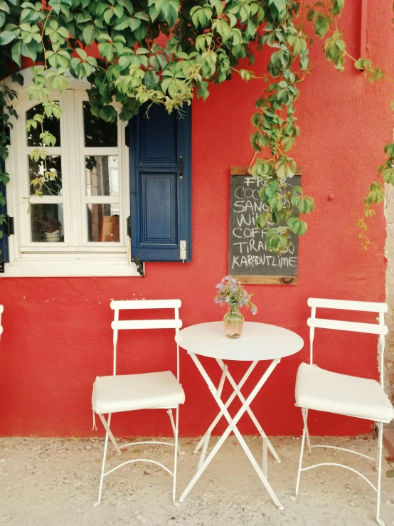 two white chairs with a white table sitting under a tree