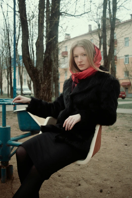 a beautiful woman wearing a black coat sitting on a park bench