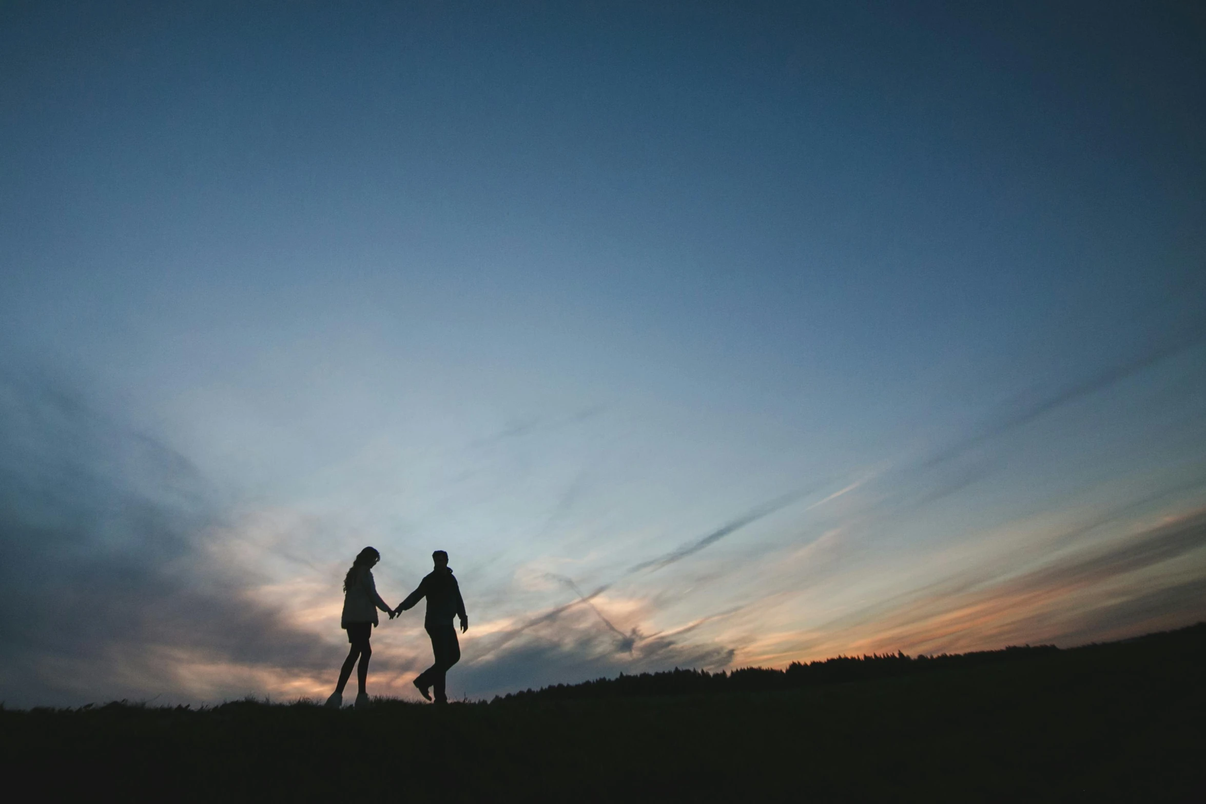 two people stand on top of a hill holding hands