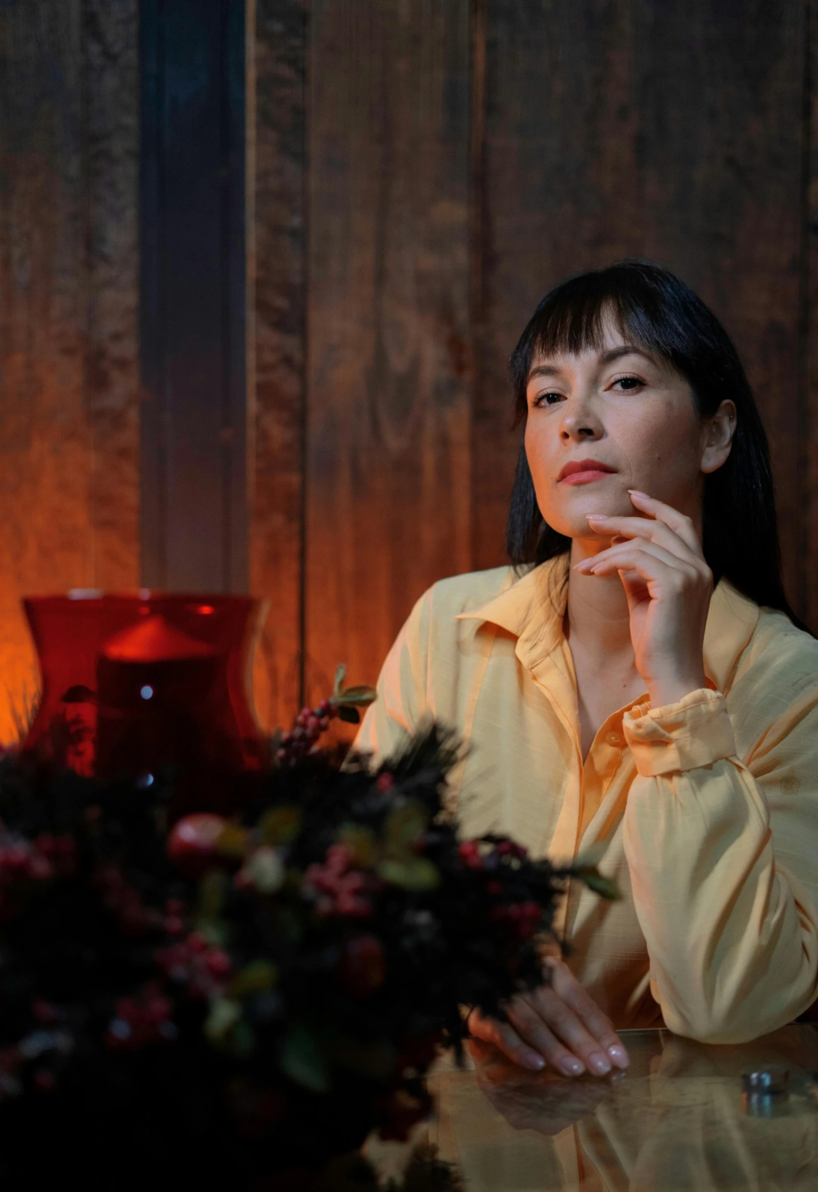 the woman sits at a glass table in front of a vase