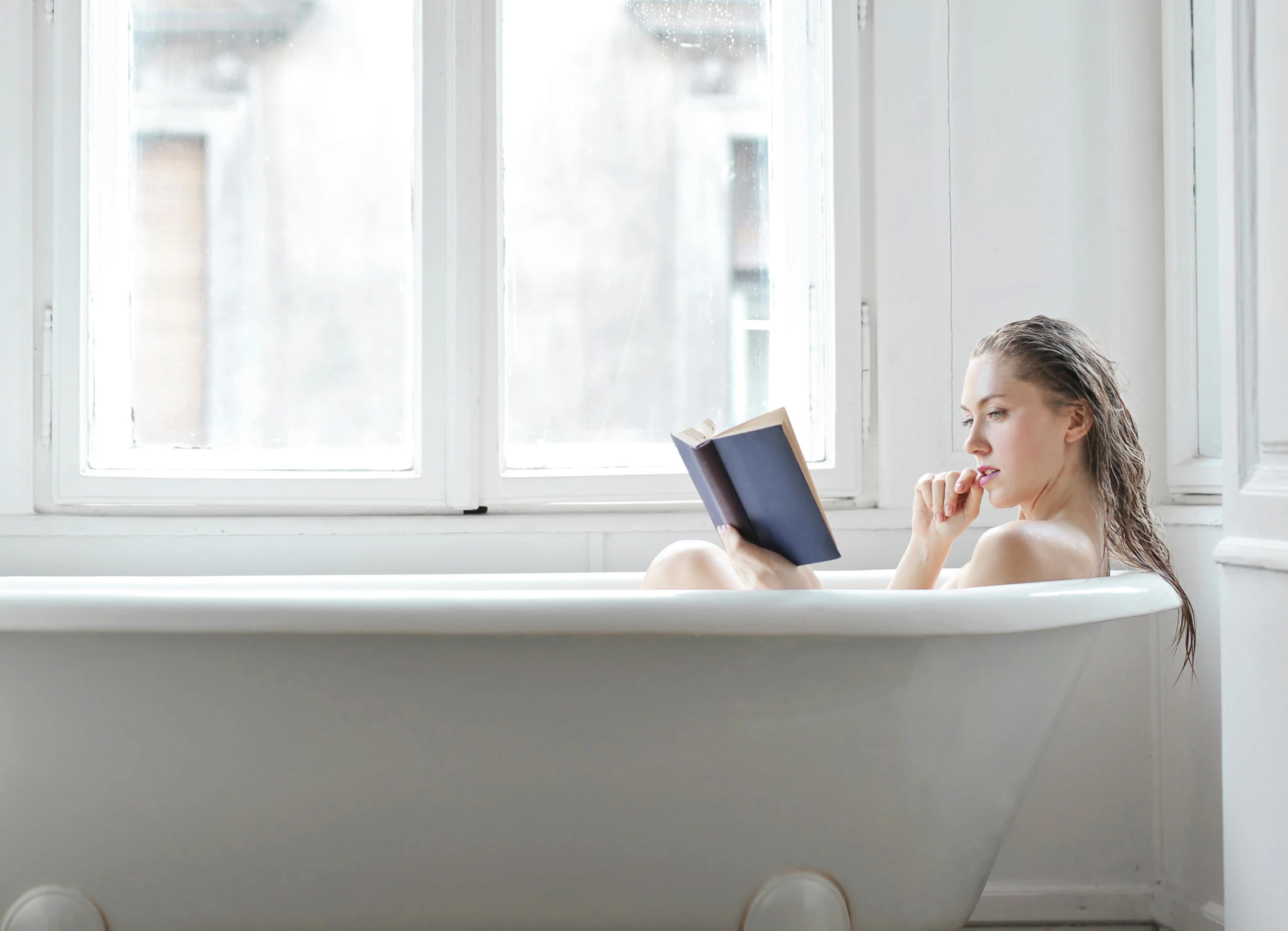 a beautiful young woman sitting in a bathtub reading a book