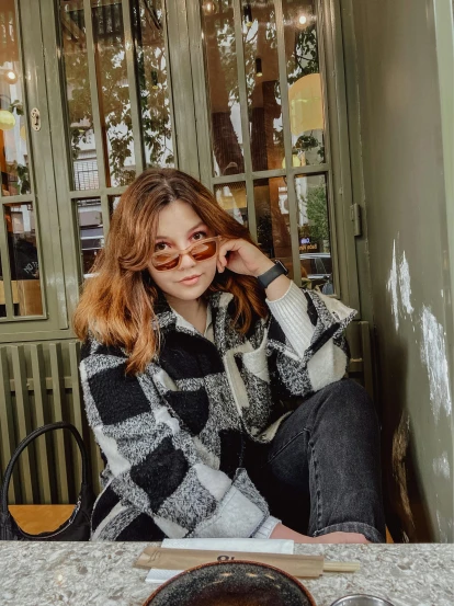 a girl wearing glasses sits at a table outside a restaurant