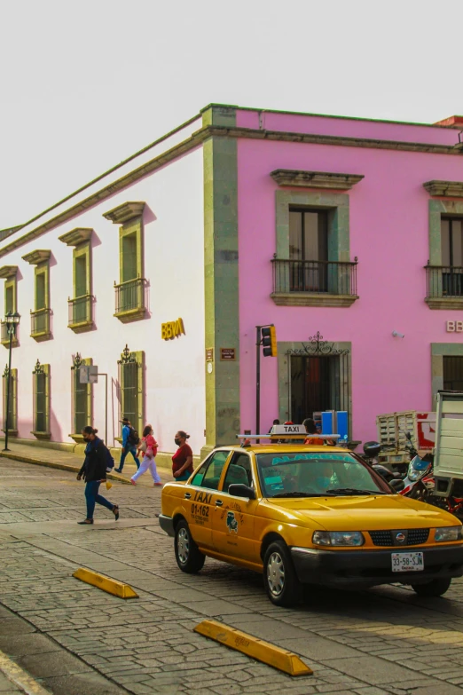 a group of people walk across the street in front of a pink building