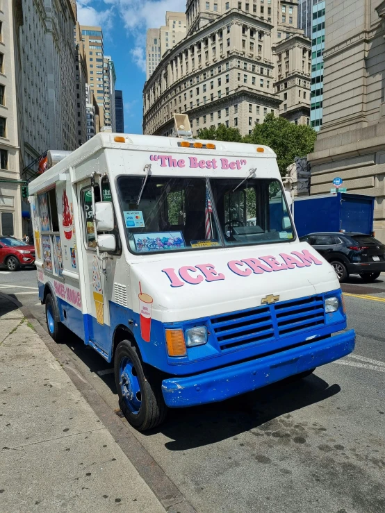 an ice cream truck driving on the street next to a tall building