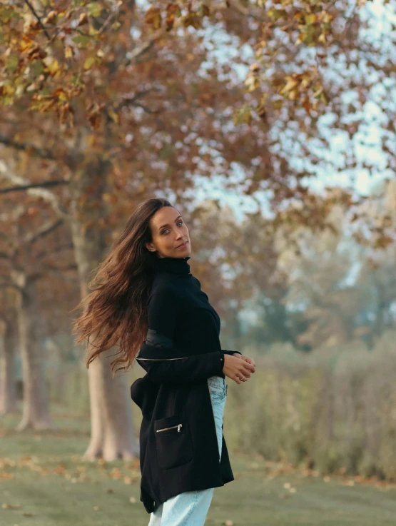 a girl wearing all black poses under a leaf filled tree