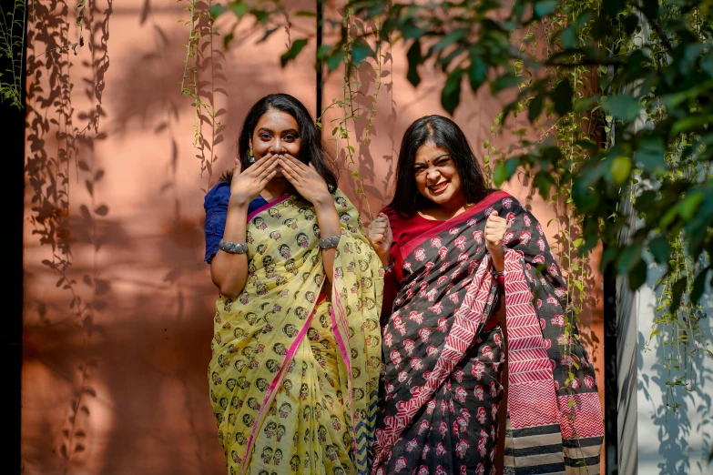 two indian women are standing by a tree