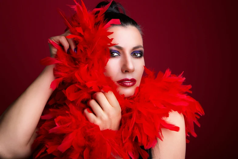 woman in black dress holding red feather over face