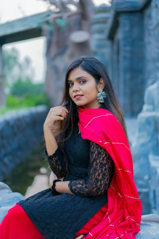 a woman sitting on a stone wall wearing a black and red outfit