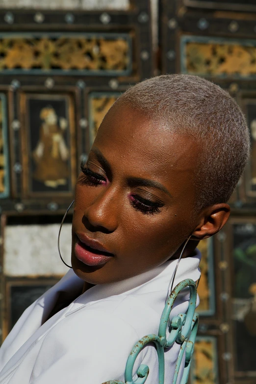 woman with painted eyes and large black earrings standing near artistic wall