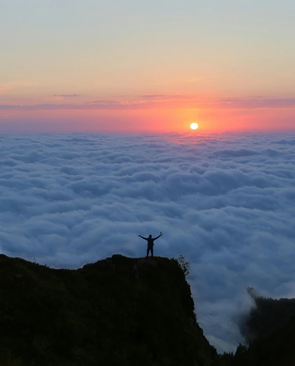 the person is standing at the top of a hill above clouds