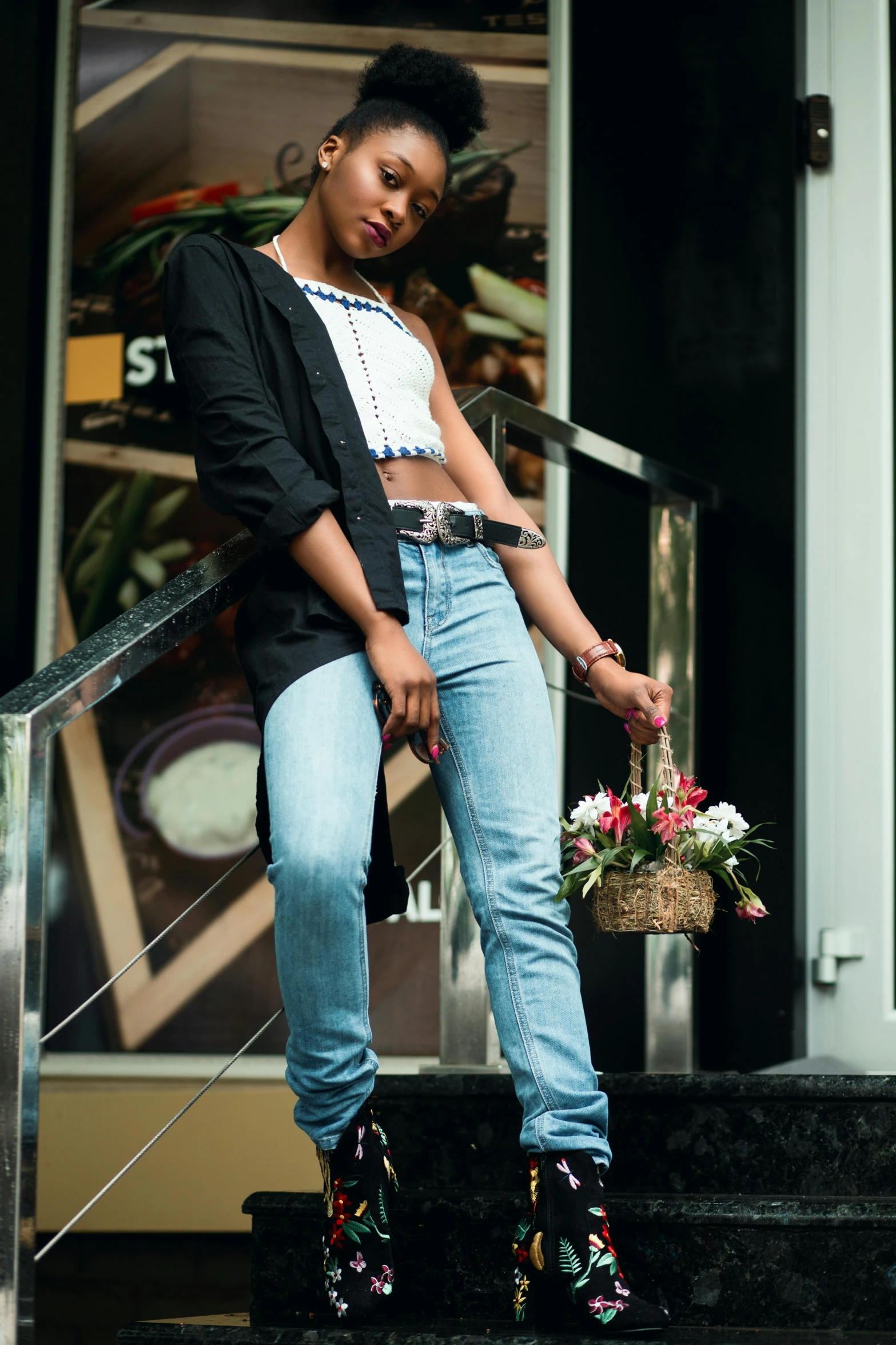 a young woman in boots, jeans, and a black cardigan stands on the steps with her basket