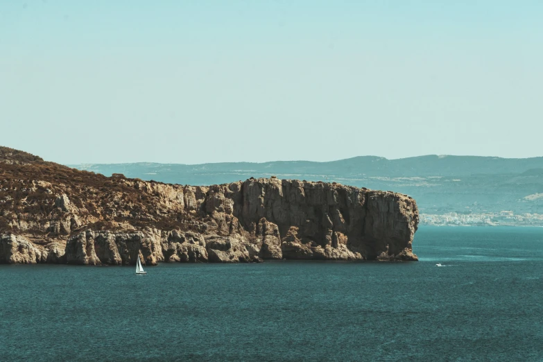 a lone sailboat out on the ocean near a rocky island