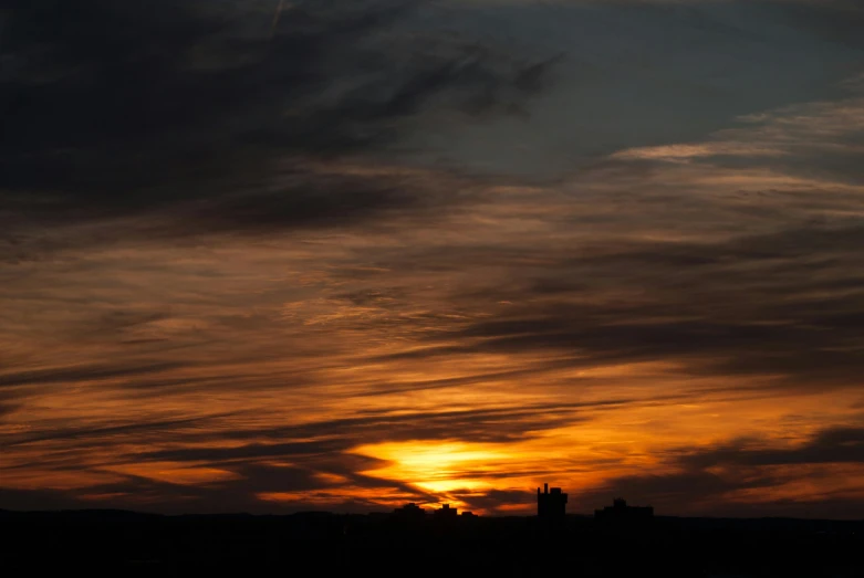 an orange sunset with white clouds over some buildings