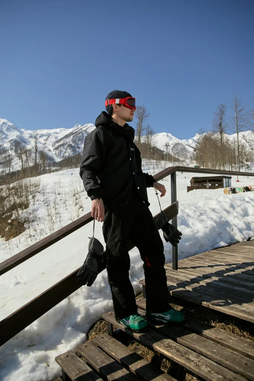 a man wearing snowboard gear standing on a wood railing