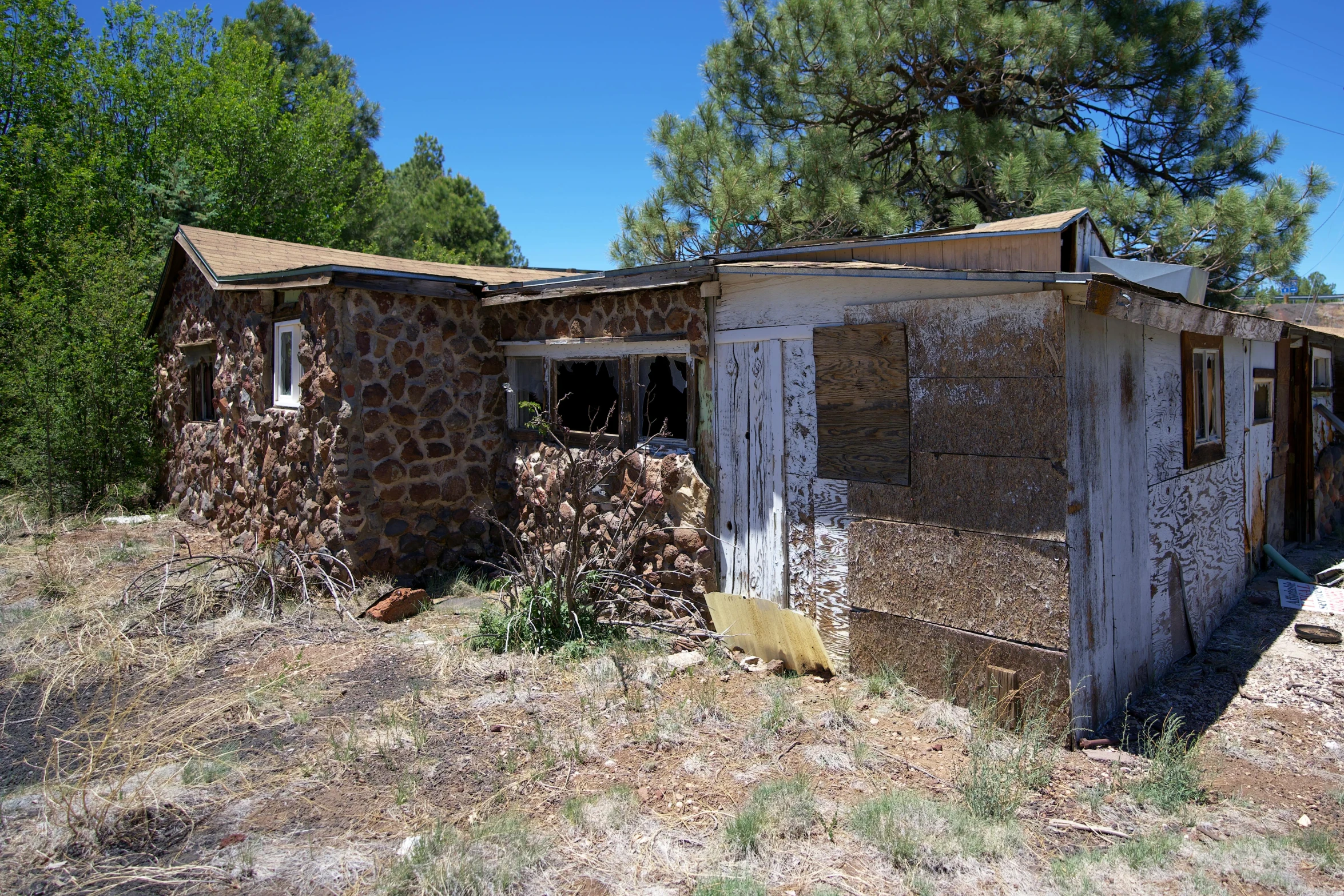 a dilapidated home in an unpaved field surrounded by trees