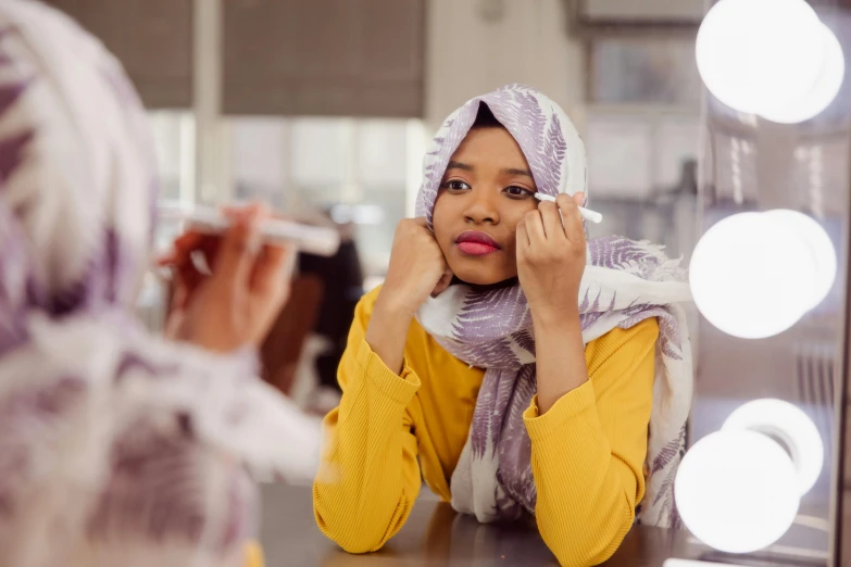 a woman putting on a makeup mirror with lights surrounding her