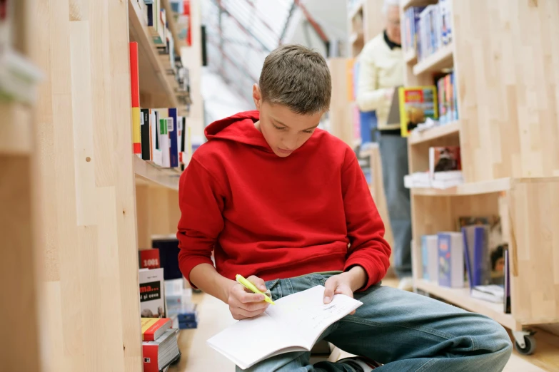 a boy sits on the floor in front of his books and writes