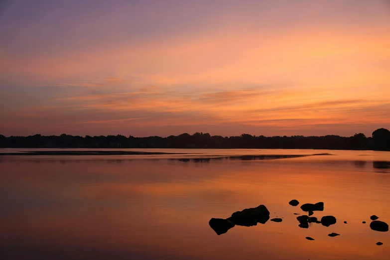 a picture of a lake at sunset with water reflection and rocks