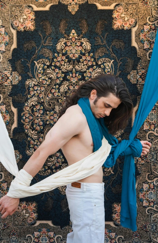 a shirtless man standing in front of a rug holding soing blue