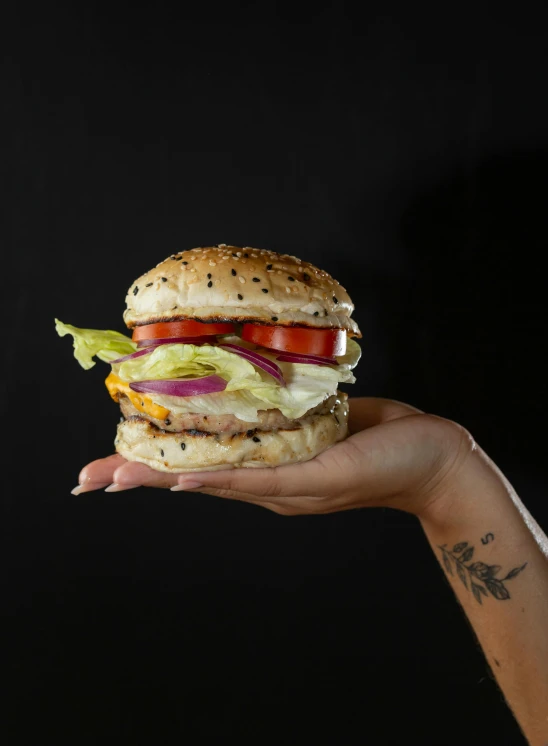 a hand holding a cheese, lettuce, tomato and onion sandwich