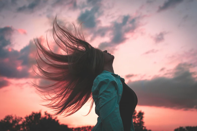 a girl with her hair in the air looking up at the sky