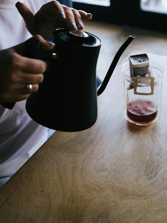 a person pours tea in a glass from a tea kettle