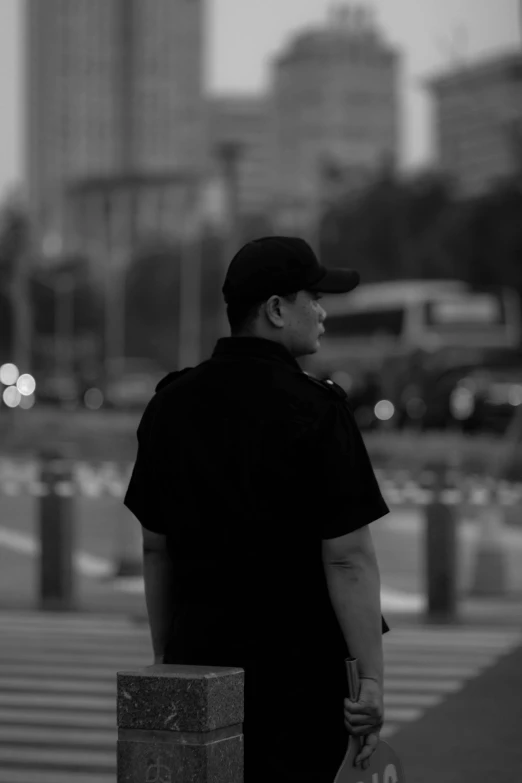 a man in a black shirt and cap stands next to a wall