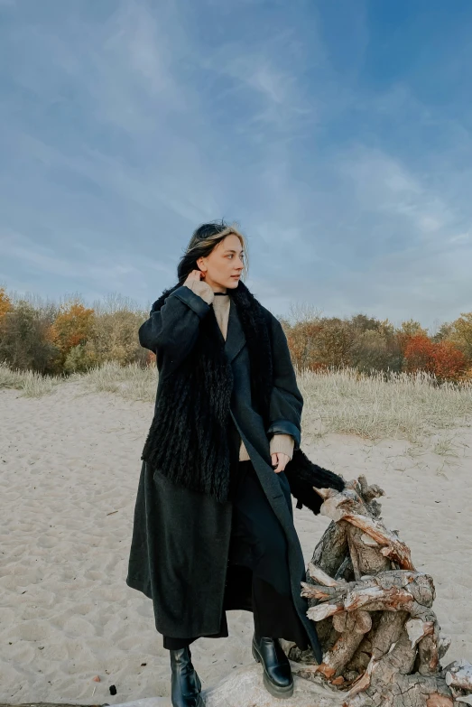 a woman in black outfit standing on sand near firewood