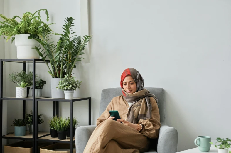 a woman in scarf holding a cell phone while sitting down