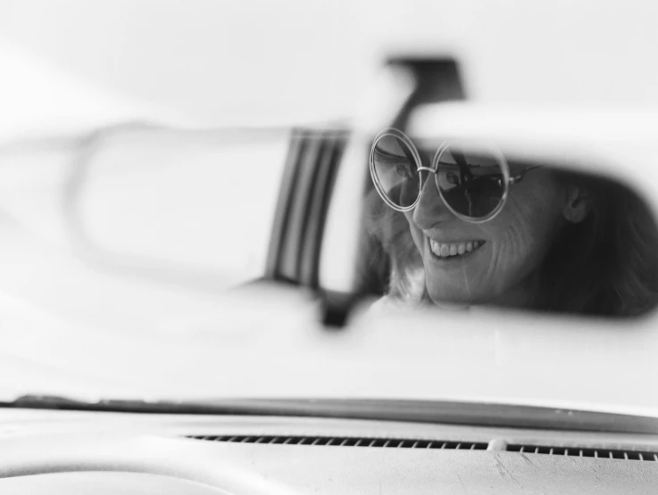 a woman in sunglasses is taking a picture through the side mirror of her car