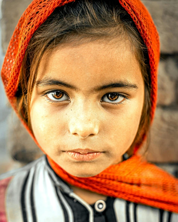 a child with large eyes wearing a bright orange hat