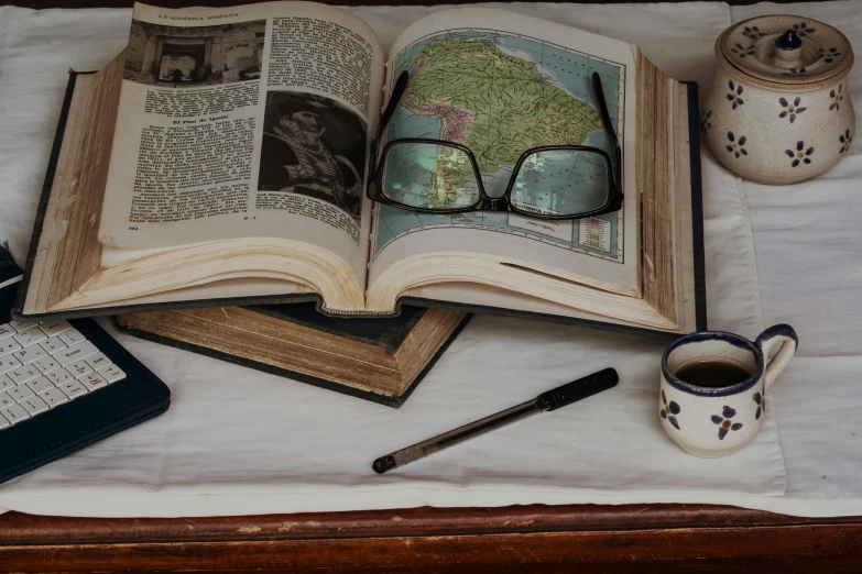 an open book with glasses on top of it next to a coffee cup