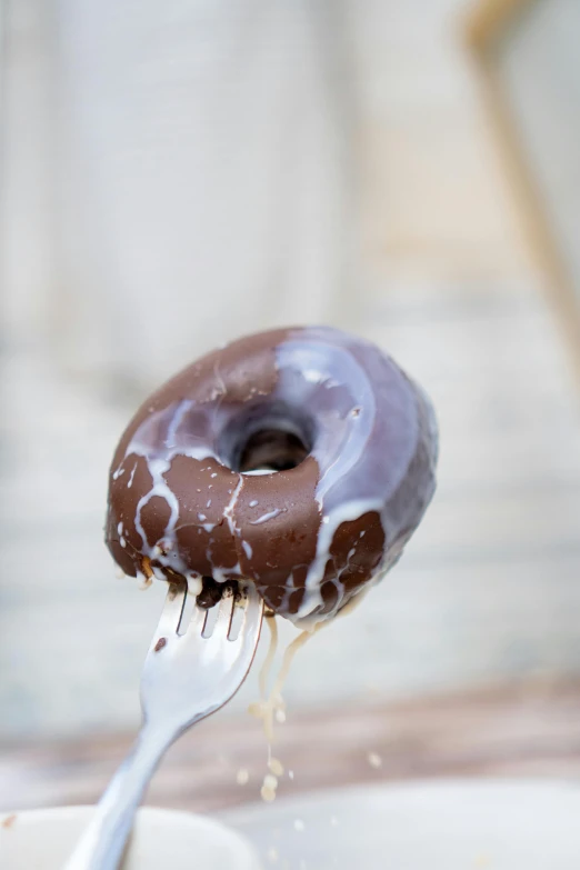 a chocolate donut covered in frosting on a fork