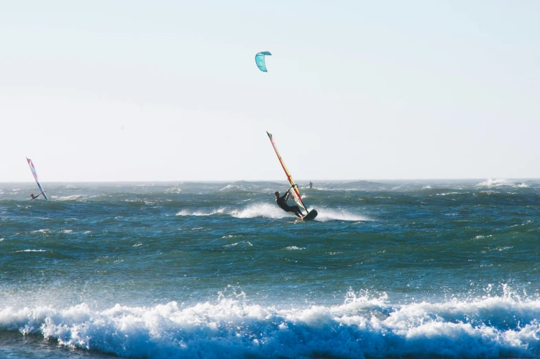 two people wind surfing in the ocean while one is gliding through the air