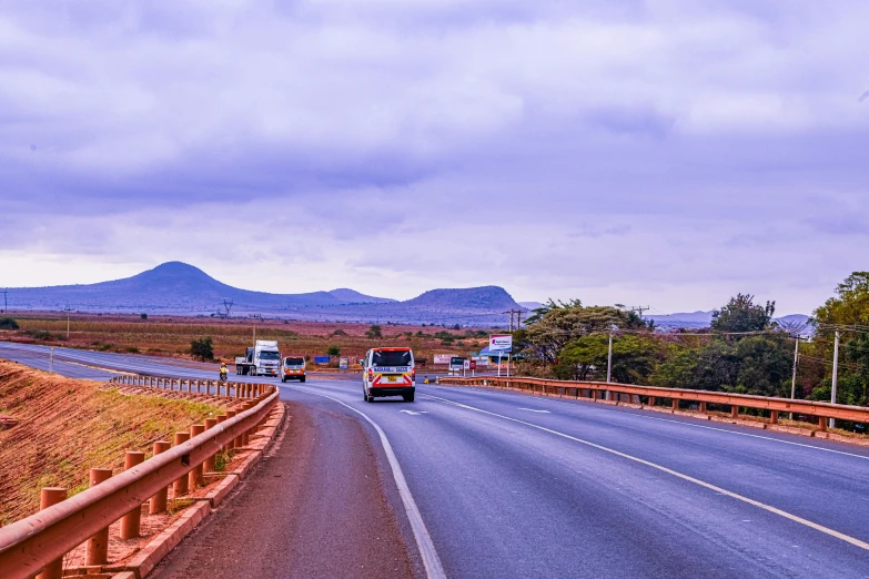 trucks on the highway next to mountains under cloudy skies