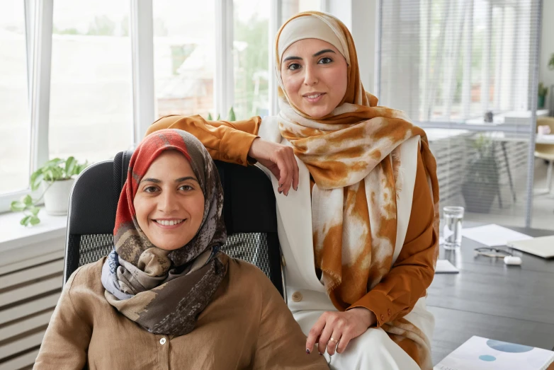 two women pose for the camera while in an office